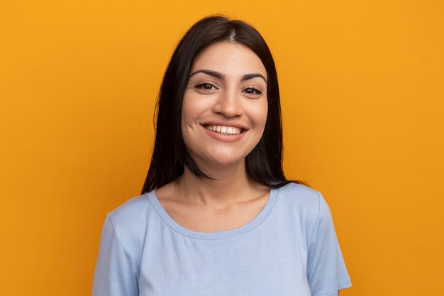 Sonriente mujer bonita morena mirando al frente aislado en la pared naranja