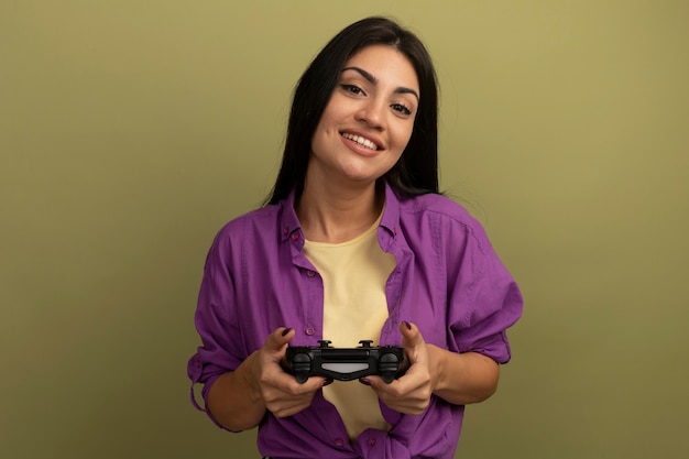 Foto gratuita sonriente mujer bonita morena tiene controlador de juego aislado en la pared verde oliva