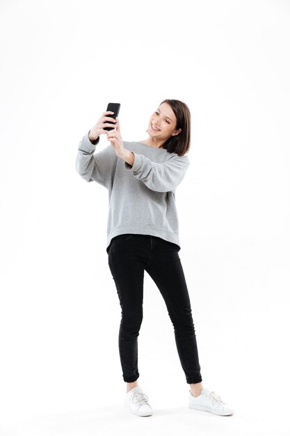 Sonriente mujer bonita de pie y tomando selfie en teléfono móvil