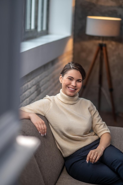 Sonriente mujer complacida sentada en el sofá mirando hacia adelante