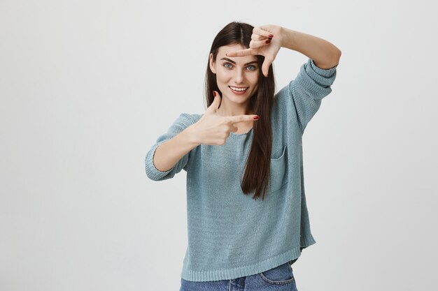 Sonriente mujer creativa haciendo marco manos, obteniendo inspiración