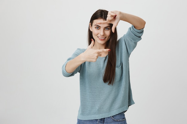 Sonriente mujer creativa haciendo marco manos, obteniendo inspiración