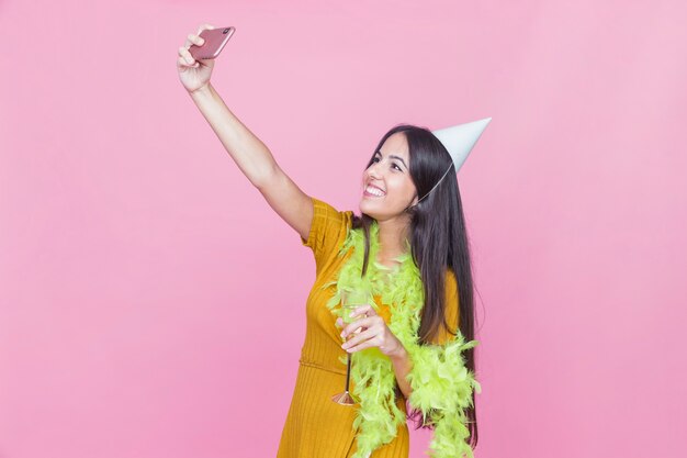 Sonriente mujer disfrutando en la fiesta tomando autorretrato sobre el fondo rosa