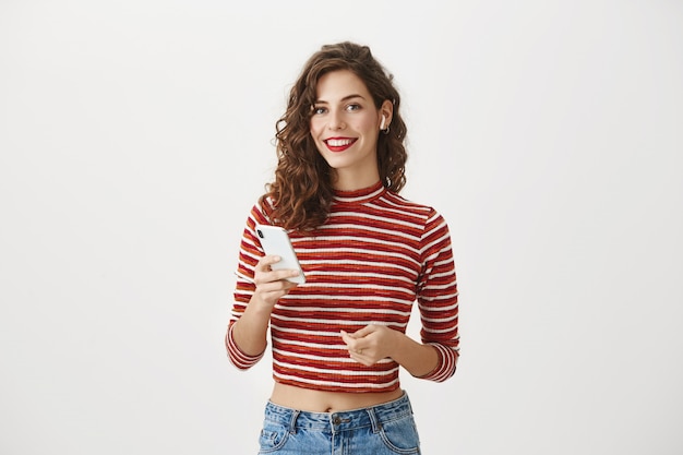 Sonriente mujer elegante con teléfono móvil, escuchando música en auriculares inalámbricos