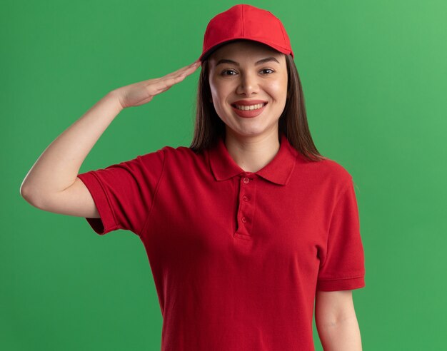 Sonriente mujer de entrega bonita en uniforme haciendo gesto de saludo