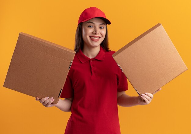 Sonriente mujer de entrega bonita en uniforme tiene cajas de pizza en dos manos
