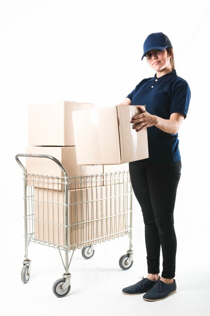 Sonriente mujer de entrega que lleva la caja del paquete delante de fondo blanco