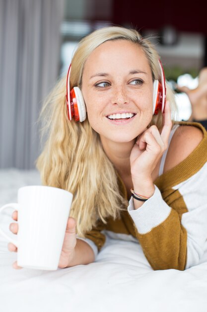 Sonriente mujer escuchando música y bebiendo té