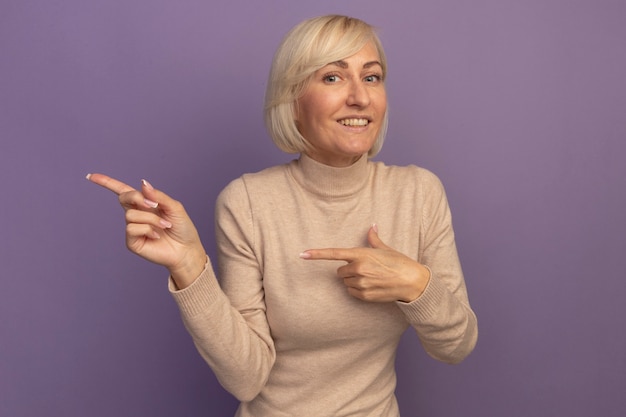 Sonriente mujer eslava bastante rubia apunta al lado con las dos manos en púrpura