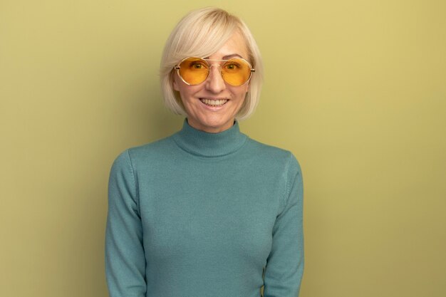 Sonriente mujer eslava rubia bonita en gafas de sol mirando a la cámara en verde oliva