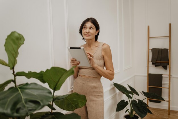 Sonriente mujer europea adulta sosteniendo tableta digital y mirando el espacio libre aislado sobre fondo blanco Tecnología de moda y concepto de personas