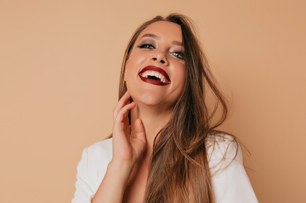 Sonriente mujer feliz con maquillaje brillante mirando a cámara mientras toca su mejilla