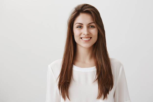 Sonriente mujer feliz de pie en camiseta casual blanca sobre gris