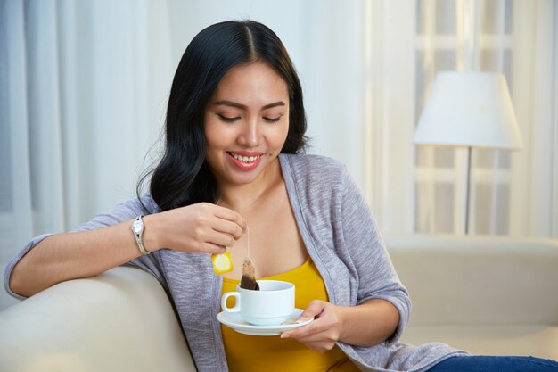 Sonriente mujer filipina elaborando té en el sofá