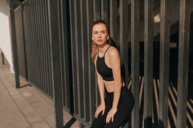 Sonriente mujer fitness en auriculares trabajando y corriendo en la plaza del deporte