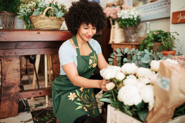 Sonriente mujer florista arreglando flores de peonía blanca