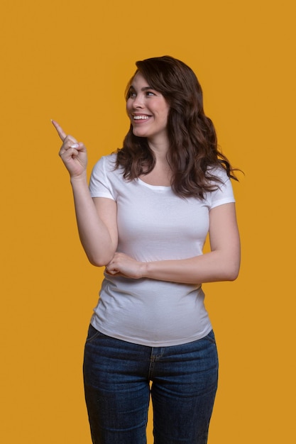 Sonriente mujer hermosa alegre vestida con una camiseta y jeans apuntando con su dedo índice hacia los lados