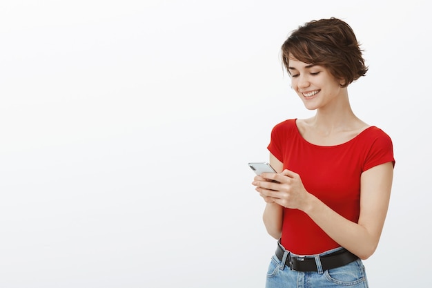 Foto gratuita sonriente mujer hermosa con aplicación de teléfono móvil, leer el mensaje con cara de satisfacción