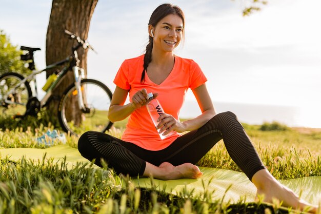 Sonriente mujer hermosa bebiendo agua en botella haciendo deporte en la mañana en el parque