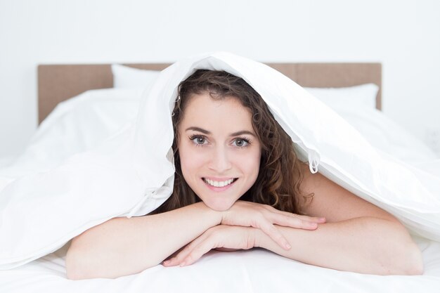 Sonriente mujer hermosa mentir bajo manta en la cama