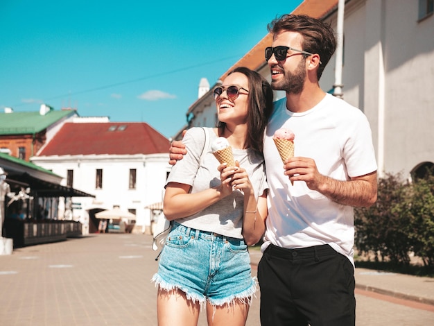 Sonriente mujer hermosa y su guapo novio Mujer en ropa casual de verano Feliz familia alegre Pareja posando en el fondo de la calle con gafas de sol Comiendo delicioso helado en cono de waffles