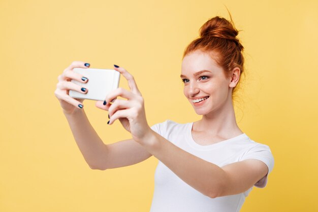Sonriente mujer de jengibre en camiseta haciendo selfie en su teléfono inteligente