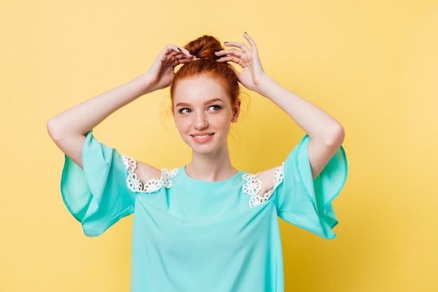 Foto gratuita sonriente mujer de jengibre en vestido corrige su cabello y mirando a otro lado