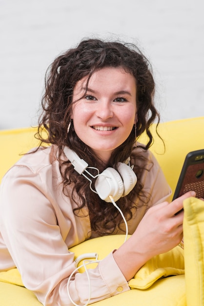 Sonriente mujer joven con auriculares alrededor de su cuello con teléfono móvil