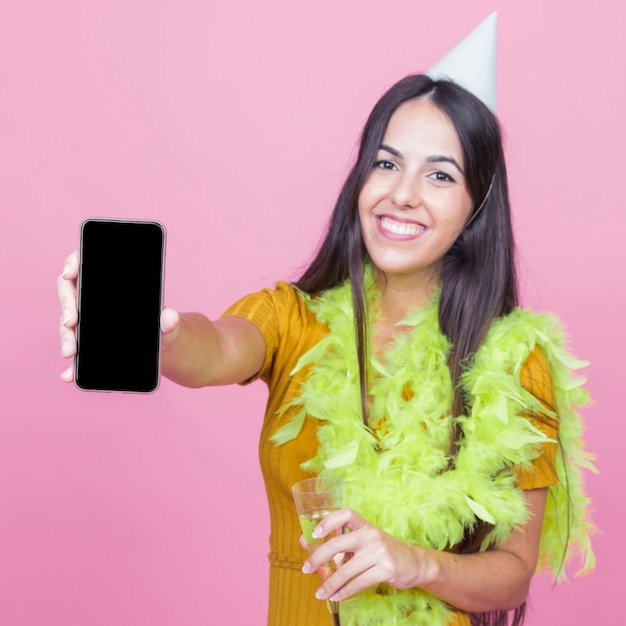 Foto gratuita sonriente mujer joven con boa y sombrero de fiesta con smartphone