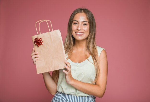 Sonriente mujer joven con bolsa de papel con lazo rojo