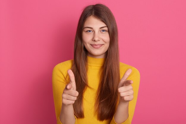 Sonriente mujer joven y bonita apuntando a la cámara con expresión facial coqueteando, se ve feliz, expresando emociones positivas, te elijo