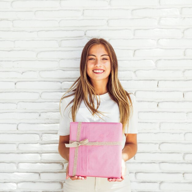 Sonriente mujer joven con caja de regalo rosa