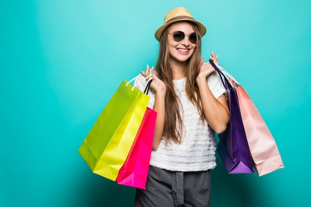 Foto gratuita sonriente a mujer joven en camiseta blanca y sombrero sosteniendo bolsas de la compra.