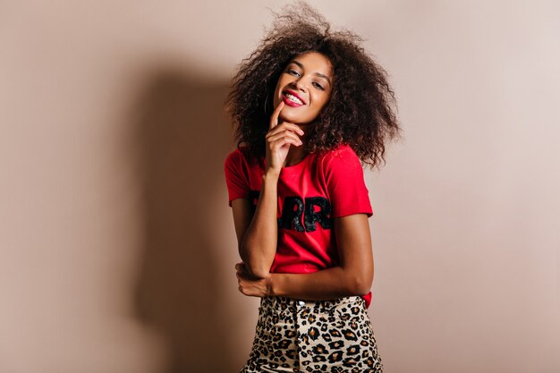 Sonriente a mujer joven en camiseta rosa de moda riendo en pared beige