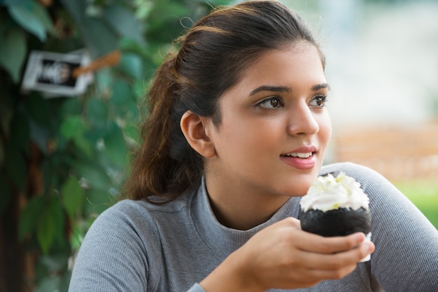 Sonriente mujer joven celebración pasteles cremosos en el café