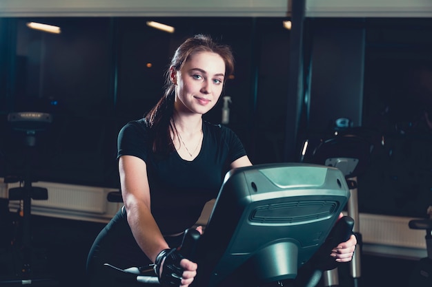 Sonriente, mujer joven, equitación, en, bicicleta estática, en, gimnasio