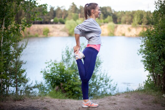 Sonriente mujer joven estirar la pierna antes de correr