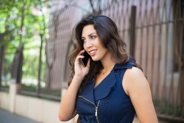 Sonriente mujer joven hablando por teléfono al aire libre
