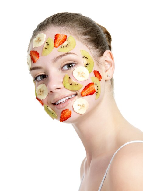 Sonriente a mujer joven hermosa con máscara de frutas en su rostro en blanco