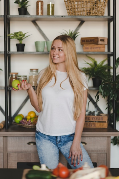 Sonriente mujer joven con manzana verde parado en frente de estante