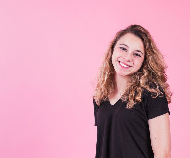 Sonriente mujer joven de pie contra el fondo rosa