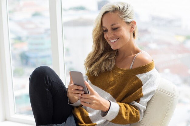 Sonriente mujer joven de redes en el teléfono en casa