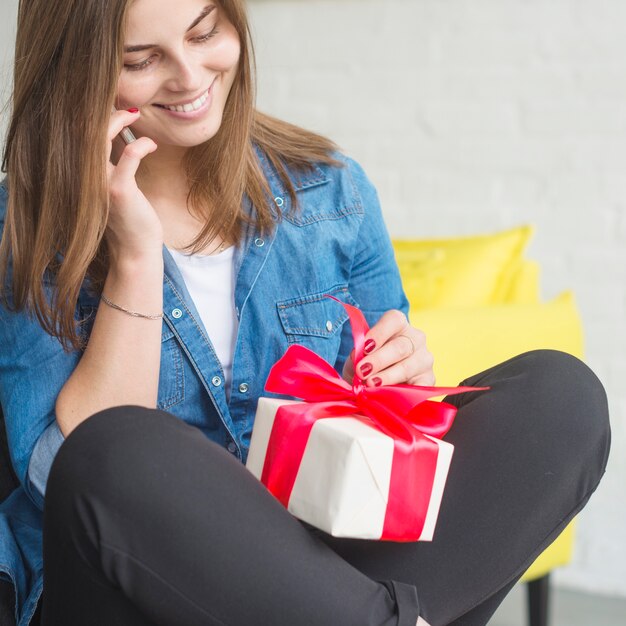 Sonriente mujer joven con regalo de cumpleaños hablando por teléfono móvil