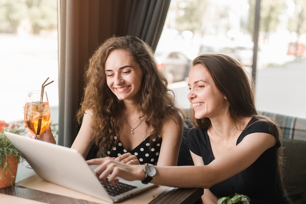 Foto gratuita sonriente mujer joven sentada en el restaurante mirando portátil