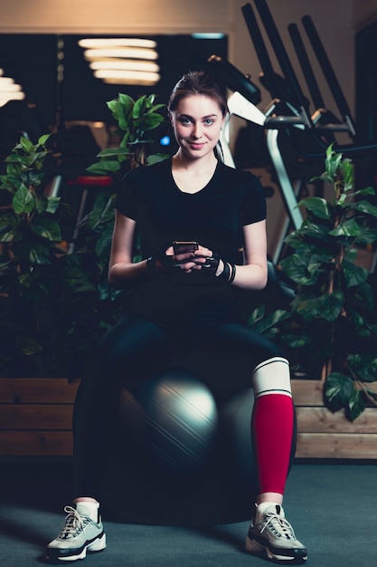 Sonriente, mujer joven, sentado, en, ejercicio, pelota, usar, teléfono celular