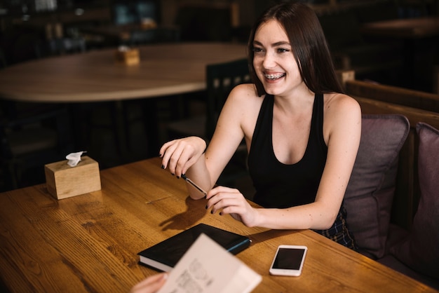 Sonriente, mujer joven, sentado, en, restaurante, tenencia, pluma, en la mano