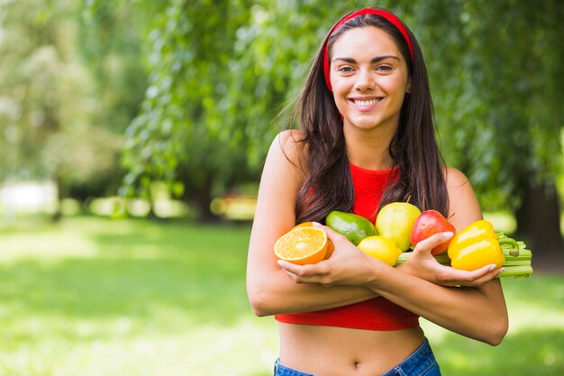 Sonriente mujer joven con verduras frescas y frutas en las manos
