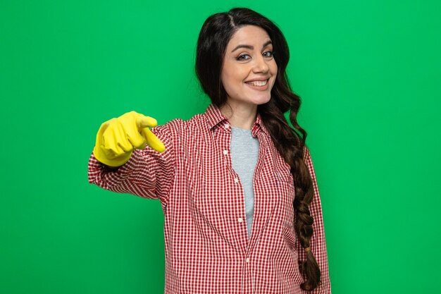 Sonriente mujer limpiador bastante caucásico con guantes de goma apuntando y mirando