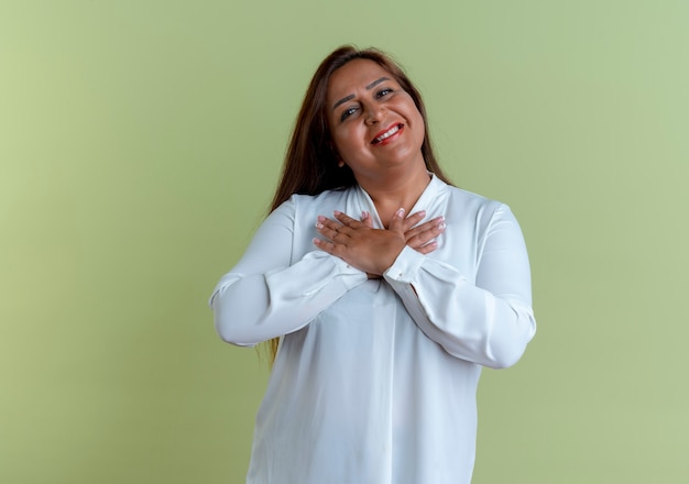 Sonriente mujer de mediana edad caucásica casual poniendo las manos en el corazón aislado en la pared verde oliva