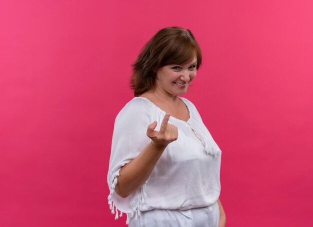 Sonriente mujer de mediana edad gesticulando ven aquí llamándote en la pared rosa aislada